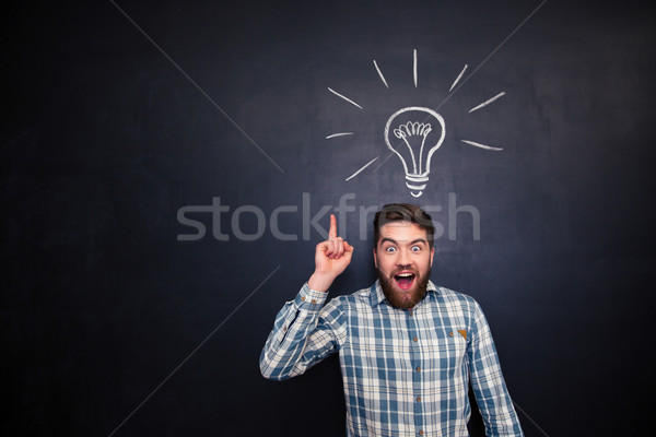 Excited man pointing up over blackboard background with light bulb  Stock photo © deandrobot