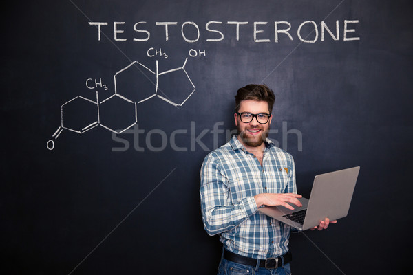 Happy scientist standing over chalkboard background and using laptop  Stock photo © deandrobot