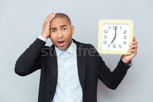 Sad shocked african man holding big clock Stock photo © deandrobot