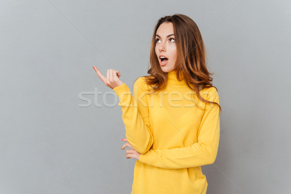 Young amazed woman in yellow sweater pointing finger away Stock photo © deandrobot
