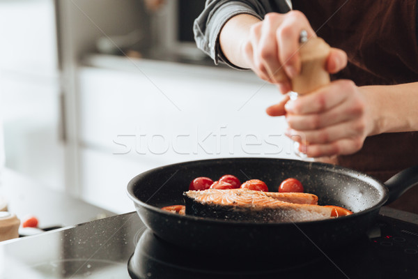 Cropped image of young woman cooking fish and tomatoes. Stock photo © deandrobot