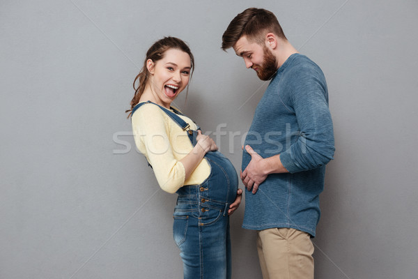 Pregnant smiling woman standing near cheerful man compare stomachs. Stock photo © deandrobot