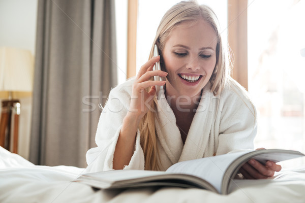 Fiatal szőke nő olvas magazin beszél telefon Stock fotó © deandrobot