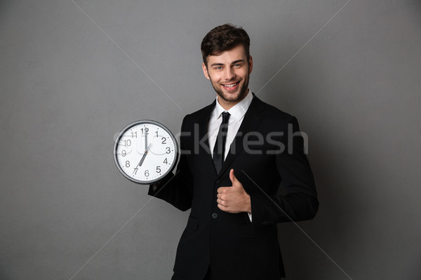 Young successful business man holding clock while showing thumb  Stock photo © deandrobot