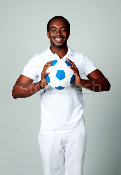 Happy african man holding soccer ball on gray background Stock photo © deandrobot