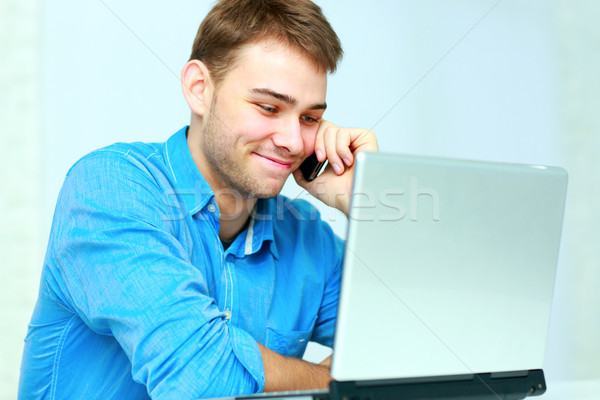 Young businessman talking on the phone and looking on laptop at office Stock photo © deandrobot