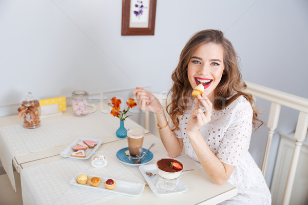 Stock photo: Happy woman eating small cakes and drinking latte in cafe