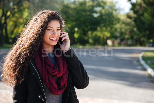 Beautiful dark-skinned young woman talking at phone Stock photo © deandrobot