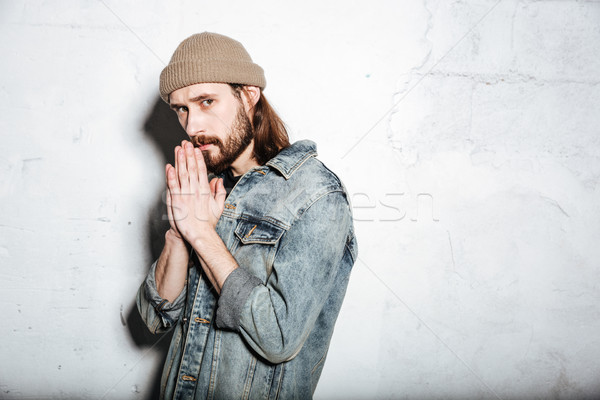 Serious bearded hipster man prays over wall background. Stock photo © deandrobot