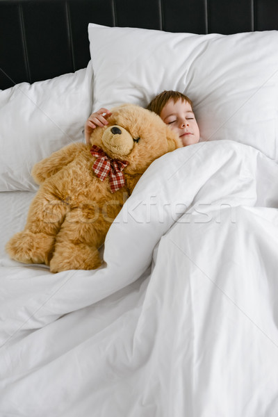 Cute boy sleeping with teddy bear in bed. Stock photo © deandrobot