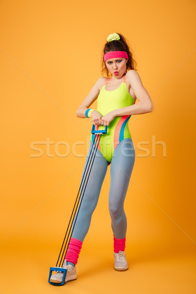 Tensed cute young fitness woman standing and exercising with expander Stock photo © deandrobot