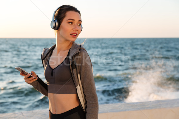 Young pretty woman in sport wear listening to music, looking asi Stock photo © deandrobot