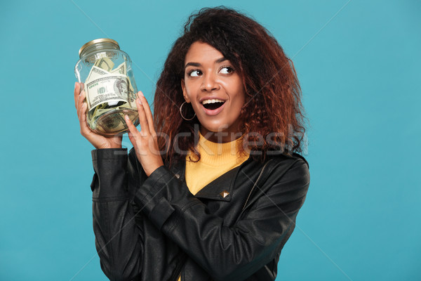Happy intrigued african woman in leather jacket holding jar Stock photo © deandrobot