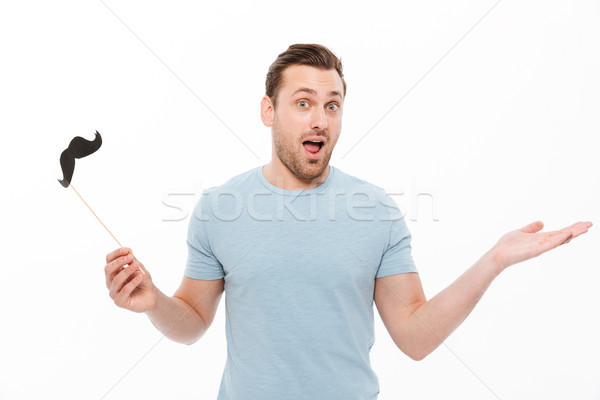 Photo of cheerful guy in casual t-shirt holding paper moustache  Stock photo © deandrobot
