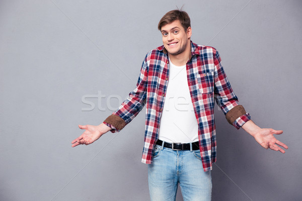 Confused cute young man standing and shrugging Stock photo © deandrobot