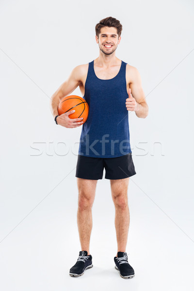 Happy young sportsman holding basketball ball and showing thumbs up Stock photo © deandrobot