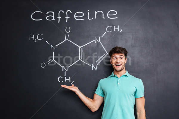 Cheerful young scientist showing chemical structure of caffeine molecule Stock photo © deandrobot