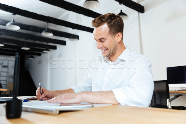 Happy businessman smiling and writing at the table Stock photo © deandrobot