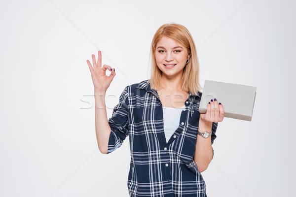 Positive young woman holding book and make okay gesture. Stock photo © deandrobot