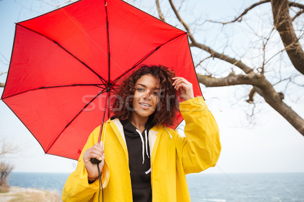 Happy african curly young lady wearing yellow coat with umbrella Stock photo © deandrobot