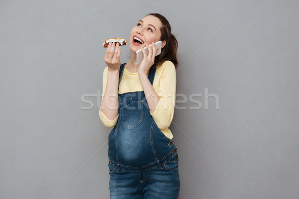 Pregnant happy woman eating eclair and talking by phone. Stock photo © deandrobot
