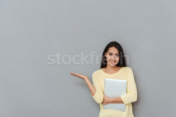 Cheerful woman with laptop standing and holding copyspace on palm Stock photo © deandrobot