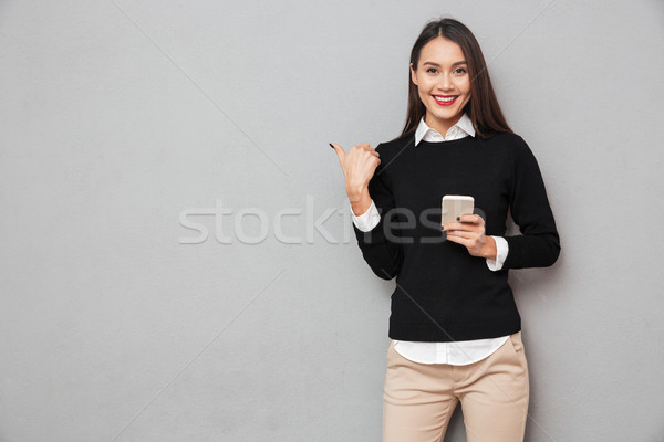 Smiling asian woman in business clothes holding smartphone Stock photo © deandrobot
