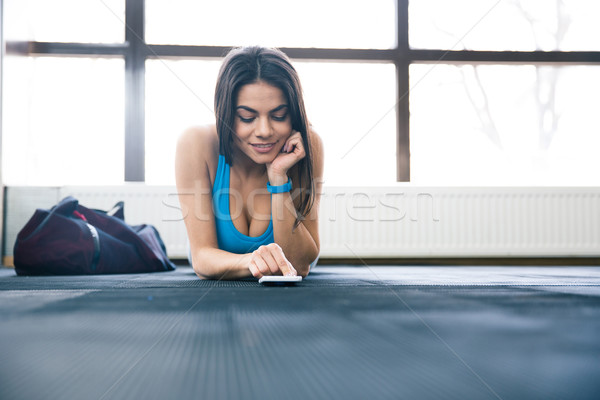 Happy sports woman lying on the floor with smartphone Stock photo © deandrobot