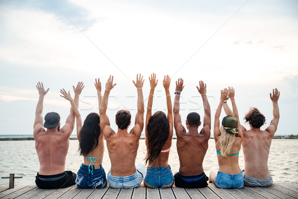Widok z tyłu ludzi posiedzenia molo podniesionymi rękami grupy Zdjęcia stock © deandrobot