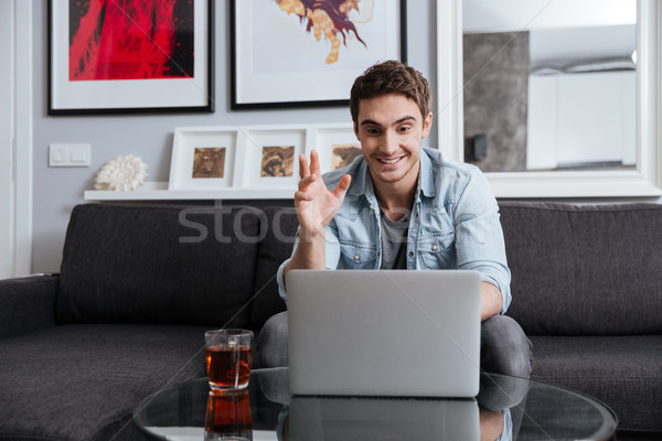 Happy young man video chatting on laptop computer at home Stock photo © deandrobot