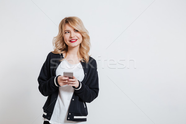 Girl in casual clothes holding mobile phone and looking away Stock photo © deandrobot