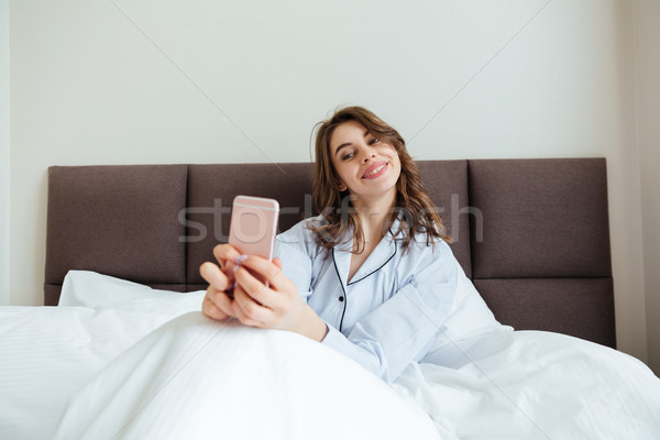Happy young lady dressed in pajama make selfie. Stock photo © deandrobot
