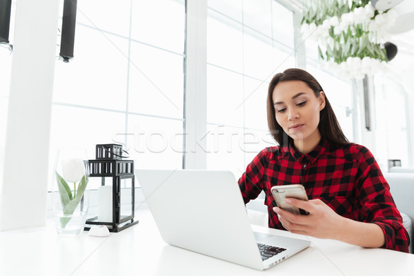 Hardworking woman using smartphone while working with laptop Stock photo © deandrobot