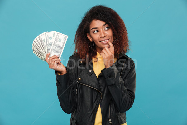 Pensive smiling african woman in leather jacket holding money Stock photo © deandrobot