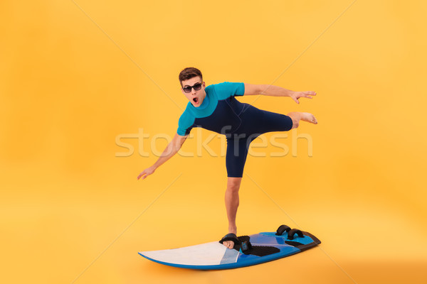 Picture of Funny surfer in wetsuit and sunglasses using surfboard Stock photo © deandrobot