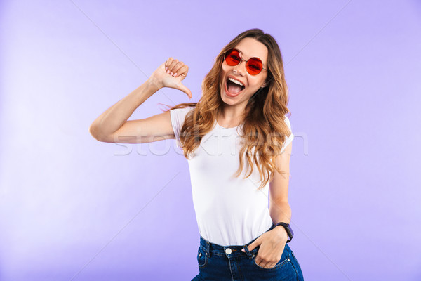 Emotional woman standing isolated over purple wall background pointing. Stock photo © deandrobot