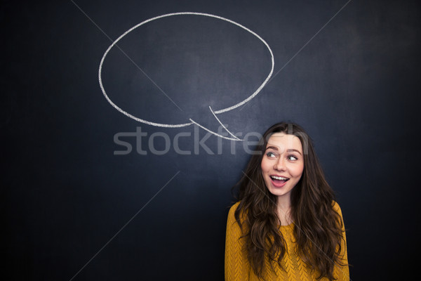 Cheerful woman smiling over blackboard with empty speech bubble Stock photo © deandrobot