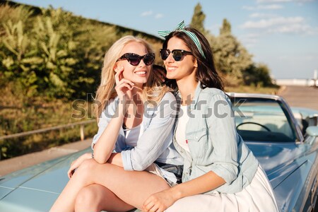Two smiling women sitting on the car hood in summer Stock photo © deandrobot
