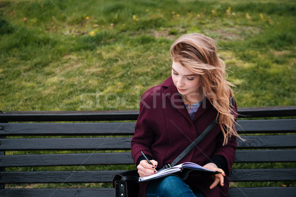 Thoughtful woman sitting on bench and writing in notebook outdoors Stock photo © deandrobot