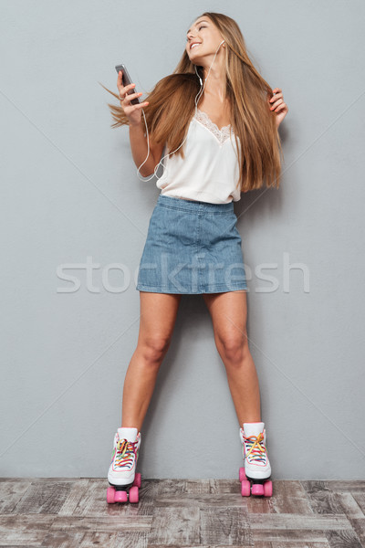 Smiling cheerful roller girl in earphones listening music Stock photo © deandrobot