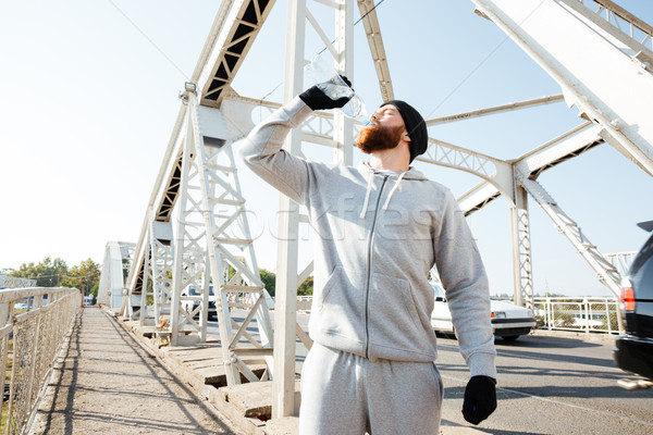 Portrait of a young bearded athlete in sportswear drinking water Stock photo © deandrobot