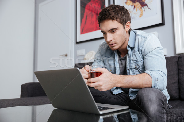 Hombre taza té mirando portátil Foto stock © deandrobot