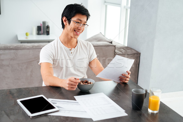 Smiling asian man working and eating Stock photo © deandrobot