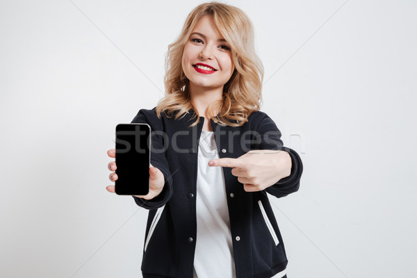 Happy young lady showing display of mobile phone and pointing. Stock photo © deandrobot