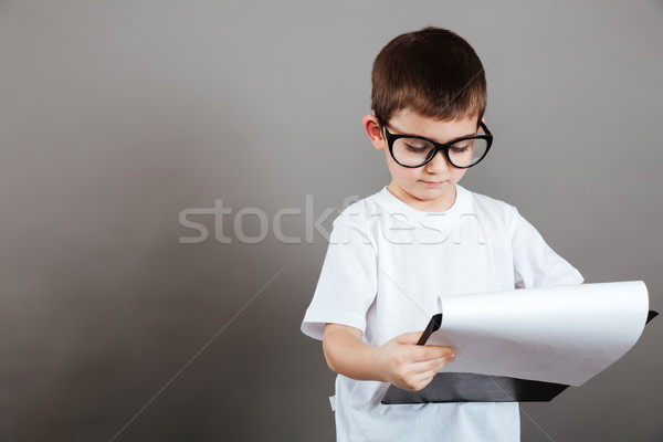 Serious little boy in glasses holding clipboard and reading documents Stock photo © deandrobot