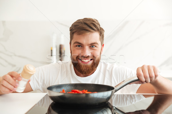Smiling bearded man sprinkle with condiments of vegetables Stock photo © deandrobot