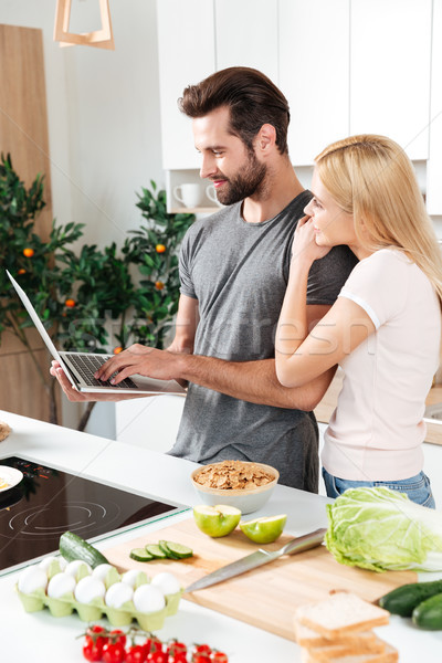 Stock photo: Smiling young loving couple cooking together using laptop