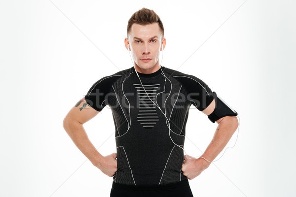Serious young sportsman in earphones standing with arms on hips Stock photo © deandrobot
