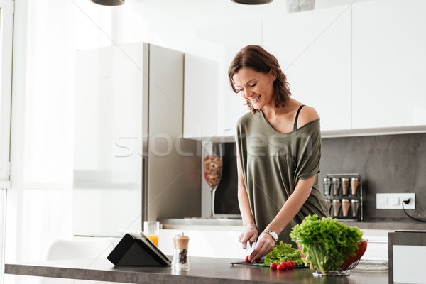 Stock photo: Smiling casual woman cuts vegetable by the table on kitchen