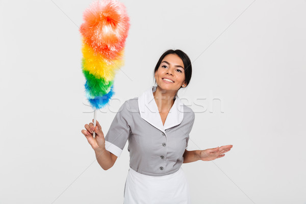 Happy brunette maid in gray uniform swipe with duster Stock photo © deandrobot